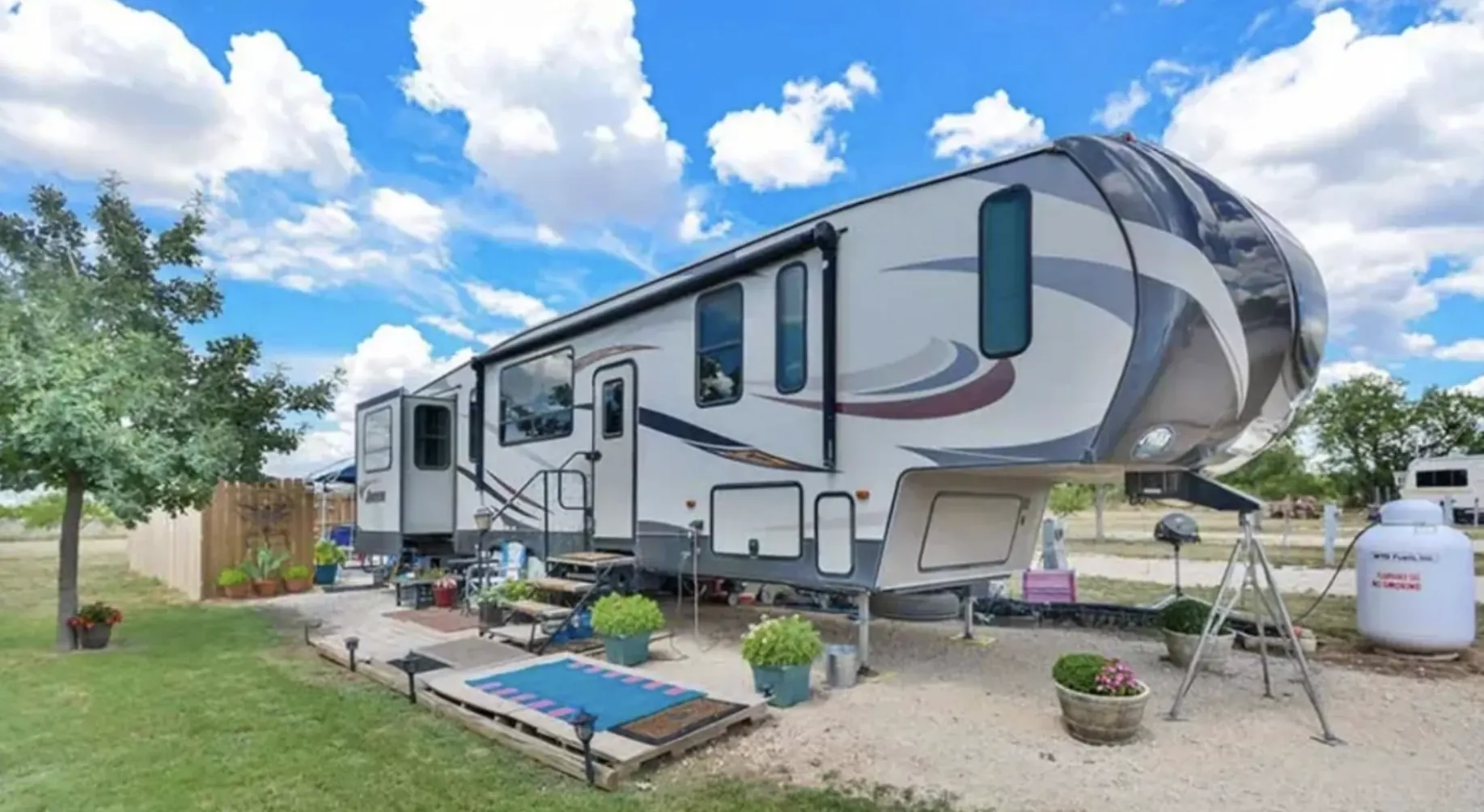 An occupied RV site with a grassy yard, privacy fence, and potted plants
